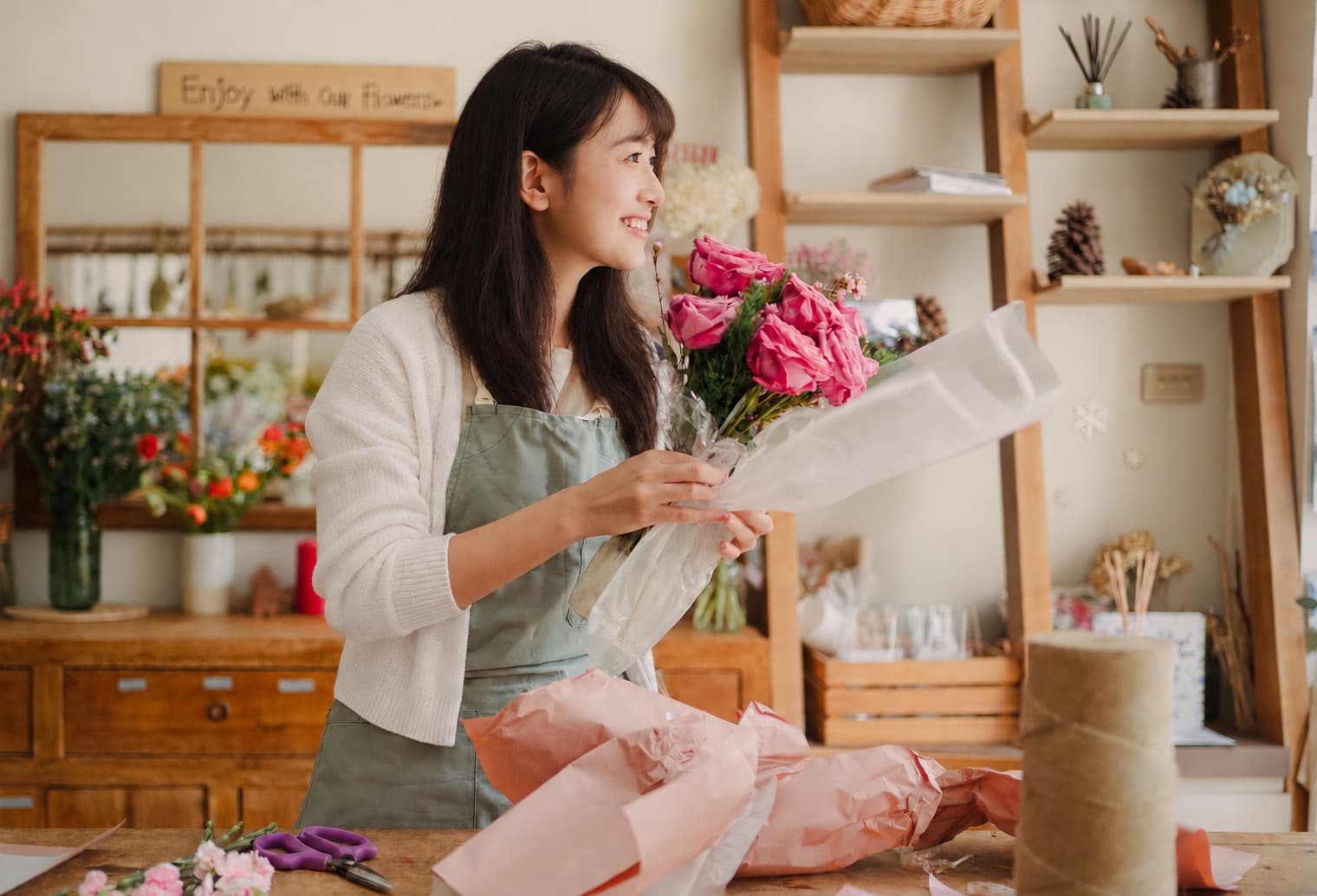 AI-edited photograph of a florist with black hair and a white cardigan wrapping pink roses
